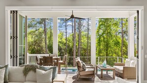 A spacious balcony with a view of a forest, furnished with a sofa, chairs, and a table. - "Watercolor Brushtrokes" Heated Private Pool/Golf Cart/ Walk to Camp Pool/Bikes (Santa Rosa Beach)
