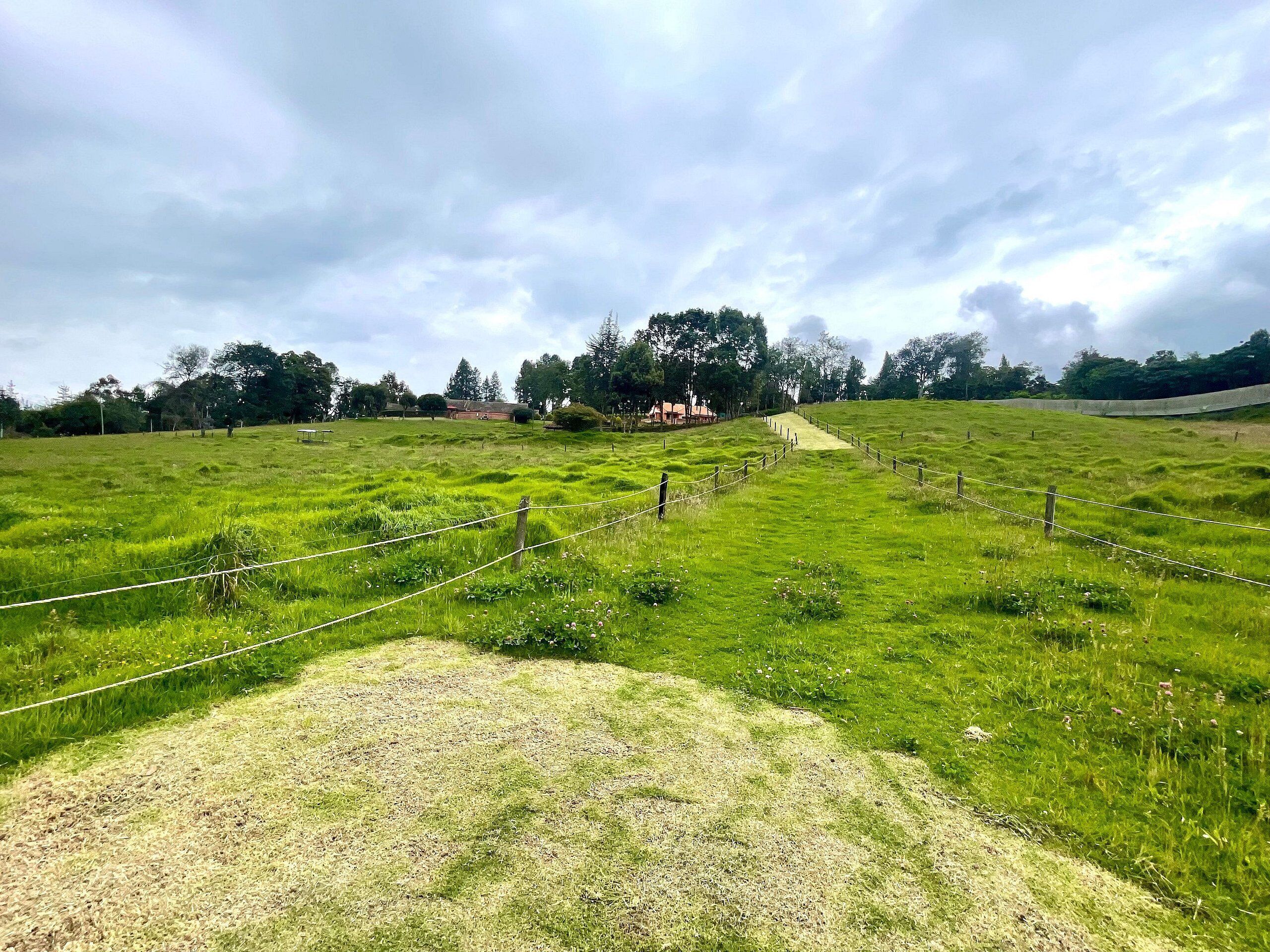 Ein grünes Feld mit einem Zaun und einem Weg, der zu einem Gebäude in der Ferne führt.