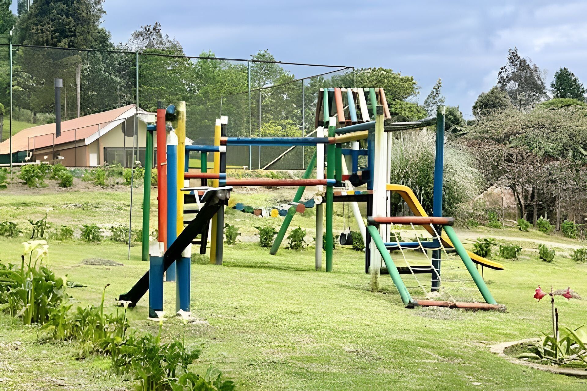 A playground with various climbing and sliding structures, surrounded by a grassy area and trees.