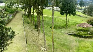 A pathway through a grassy area with trees, a small bridge, and a gazebo.