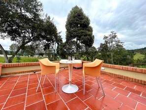 Un patio al aire libre con una mesa redonda y dos sillas, rodeado de un suelo de baldosas rojas y una pared de ladrillo.