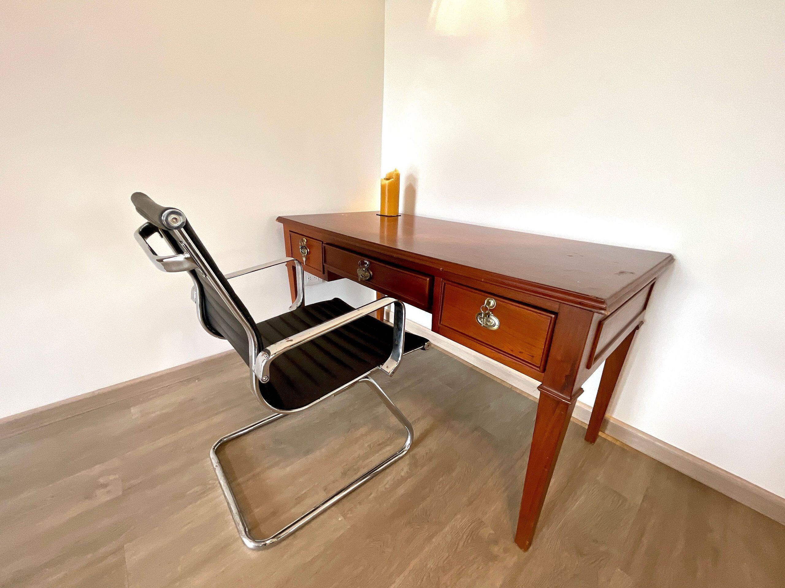 A wooden desk with a black office chair and a candle on it.