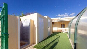 A covered outdoor area with a green artificial turf, a metal gate, and a building with a tiled roof. - Casa Rural el Olivo centenario (Perin)