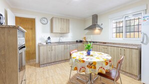 A kitchen with wooden cabinets, a built-in oven, a sink, and a dining table with chairs. - Casa Rural el Olivo centenario (Perin)