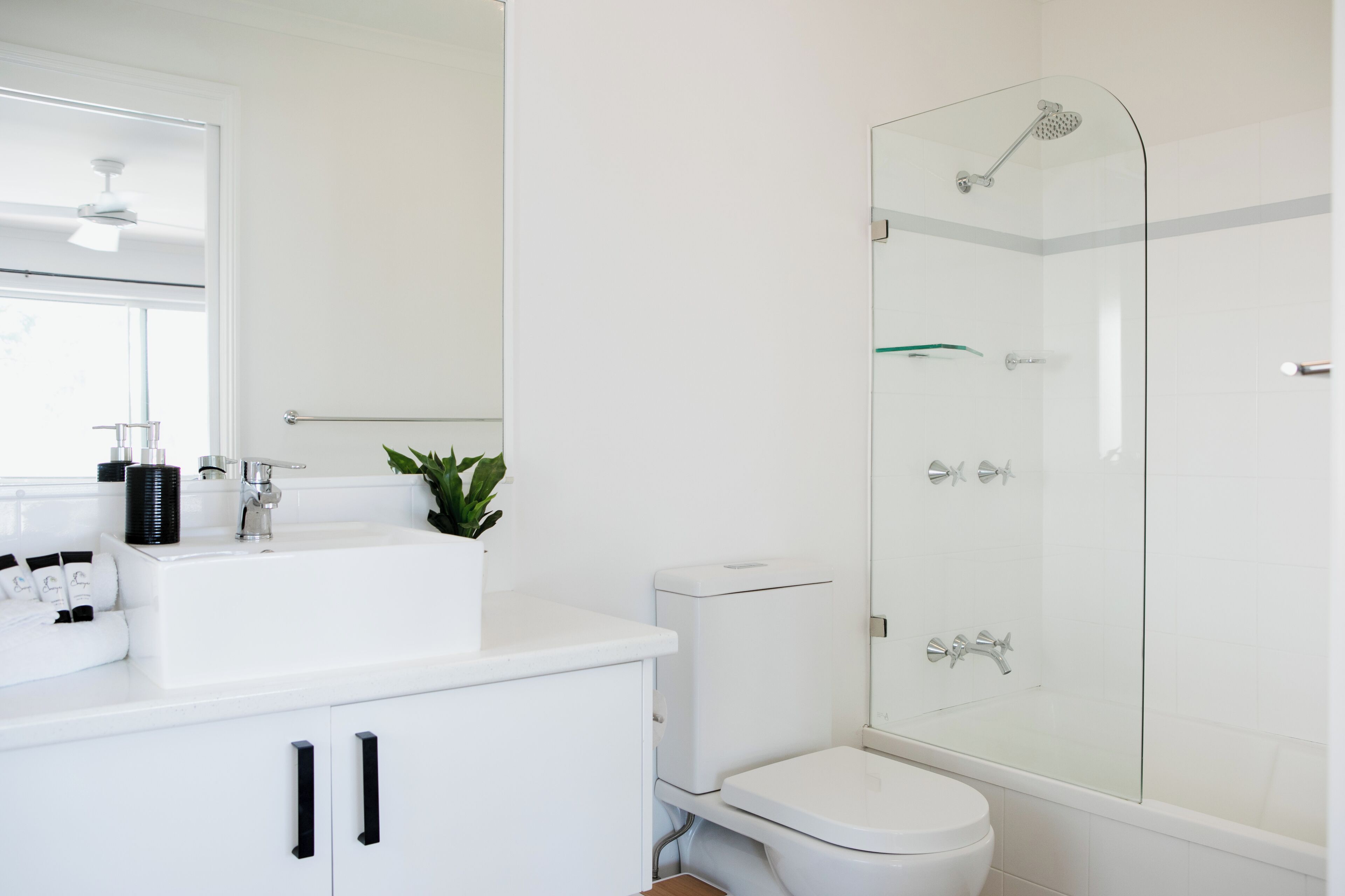 A modern bathroom with a glass-enclosed shower, a white sink with black handles, and a toilet.