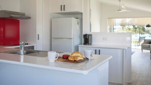 A modern kitchen with white cabinetry, a red accent wall, a stainless steel sink, and a breakfast setup with croissants and strawberries. - Lazy Days by Stay Noosa (Noosaville)