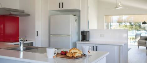 A modern kitchen with white cabinetry, a red accent wall, a stainless steel sink, and a breakfast setup with croissants and strawberries.