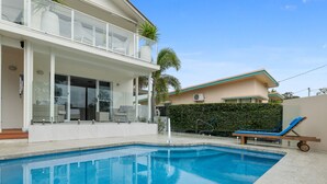 A swimming pool with a sun lounger and a covered seating area. - Lazy Days by Stay Noosa (Noosaville)