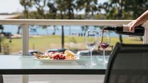 A table with a plate of food and two wine glasses, with a person pouring wine into one of the glasses. - Lazy Days by Stay Noosa (Noosaville)
