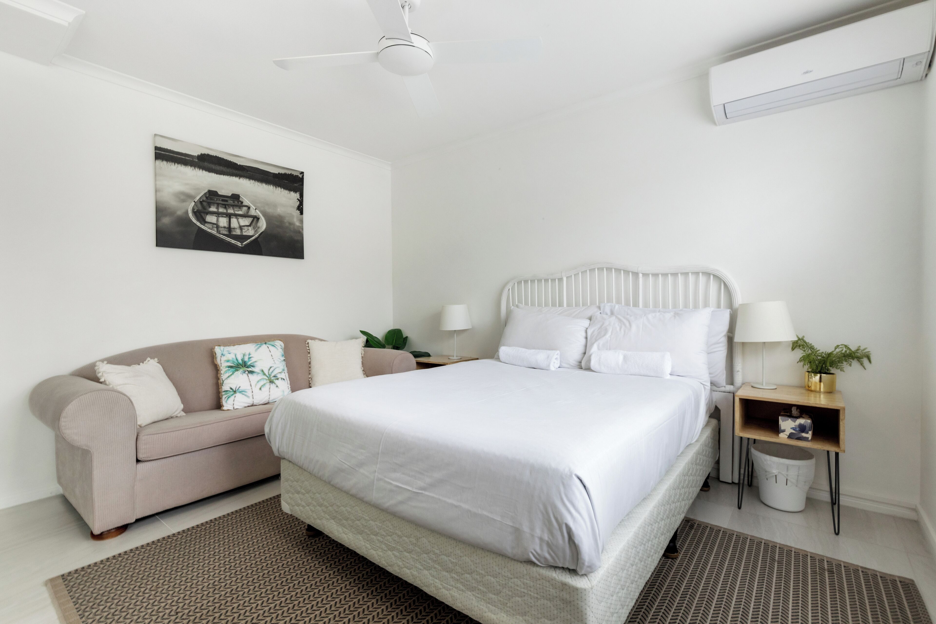 Quarto com cama, sofá, mesa de cabeceira, abajur e ar condicionado fixado na parede.