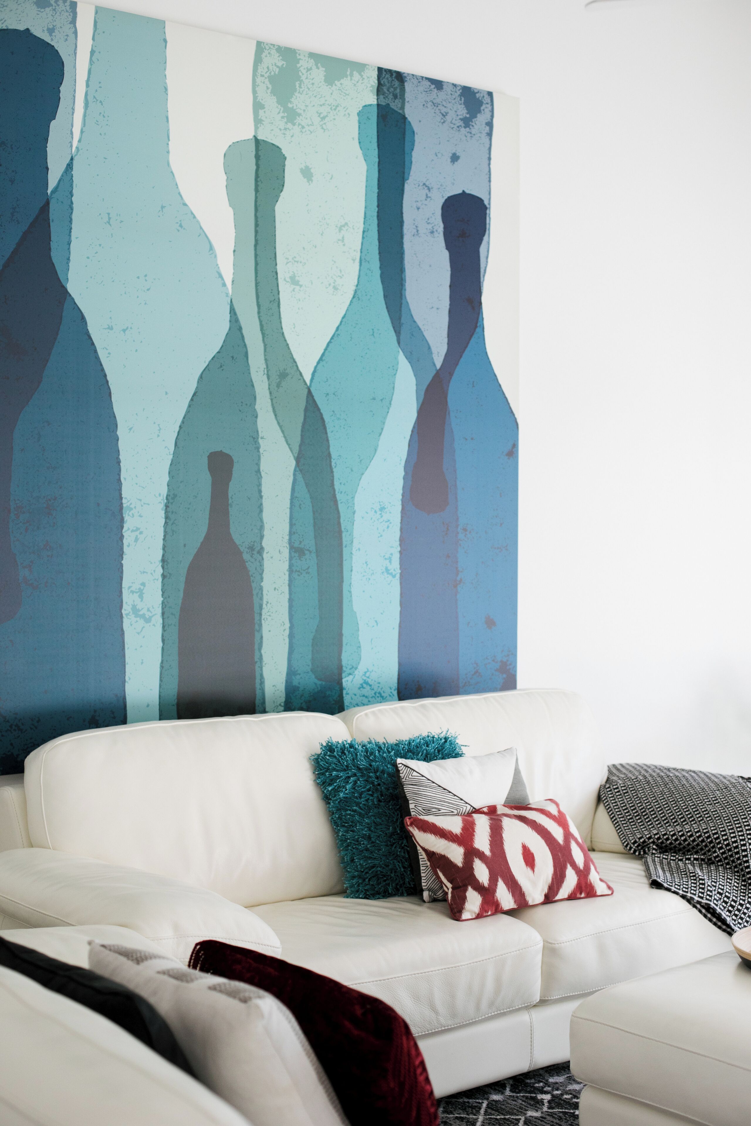 A white leather sofa with patterned pillows, a large abstract painting on the wall, and a black and white patterned throw blanket.