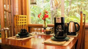 A kitchen counter with a coffee maker, a kettle, and a vase with red flowers. - Private Rainforest Retreat in Volcano Village (Volcano)