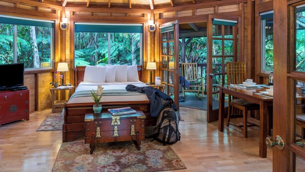 A wooden room with a bed, a desk, and a TV. - Private Rainforest Retreat in Volcano Village (Volcano)