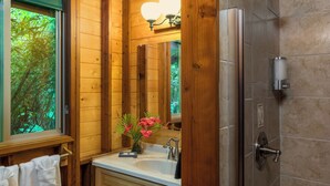 A wooden bathroom with a sink, mirror, and shower. - Rainforest Retreat in Volcano Village (Volcano)