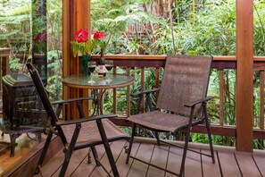 A wooden deck with wicker chairs and a glass table, surrounded by lush greenery. - Private Suite in Volcano Village Bed and Breakfast (Volcano)