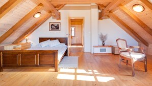 Ein gemütliches Schlafzimmer im Dachgeschoss mit Holzbalkendecke, einem Bett, einem Sessel und einem kleinen Tisch.