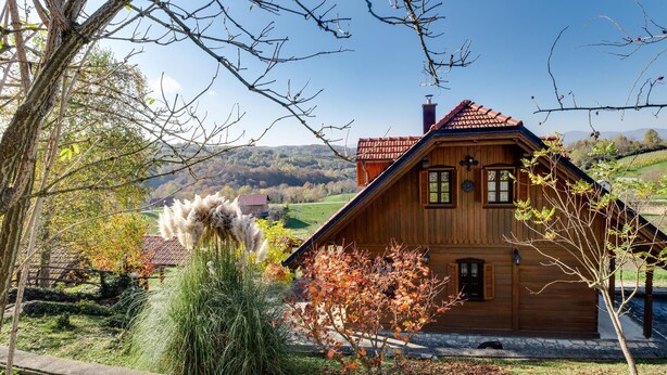Ein Holzhaus mit geneigtem Dach, einem Steinfundament und Blick auf ein grünes Tal.