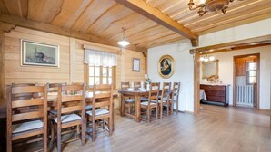 Ein Esszimmer aus Holz mit einem großen Tisch, Stühlen, einer Chandelier und einem Gemälde an der Wand.