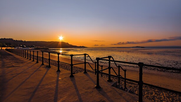 A sunset view from a seaside promenade with a metal railing and steps leading to the beach. - Funky Studio Near The Beach (Burntisland)