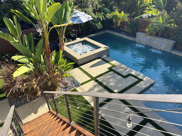 A swimming pool with a wooden deck, a small water feature, and lush tropical plants.