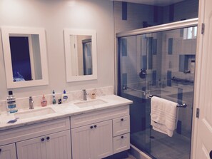 Features a dual sink vanity with ample storage, a glass-enclosed shower, and a large mirror.