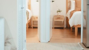 Un dormitorio con dos camas, una mesita de noche, un aparador y una puerta que da a otra habitación.