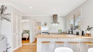 Una cocina moderna con una isla de madera, taburetes blancos y vistas al dormitorio contiguo.
