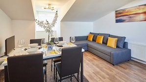 A dining area with a table set for four, a sofa with cushions, and a painting on the wall.