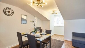 A dining area with a table set for four, a clock, a mirror, and a vase of white flowers.