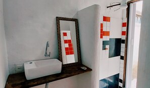 Baño con lavamanos blanco, espejo y estante.