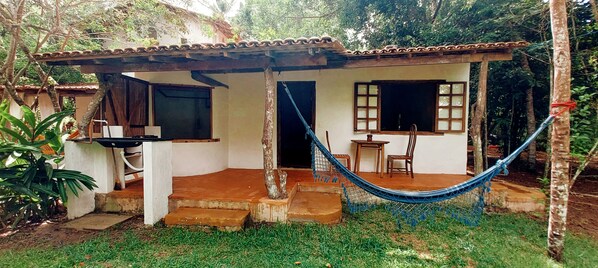 Una casita con techo de tejas, una hamaca y un patio con escalones que llevan a la entrada.