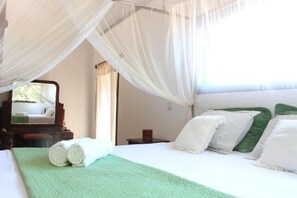 Una cama bien hecha con un edredón verde, almohadas blancas y un dosel.