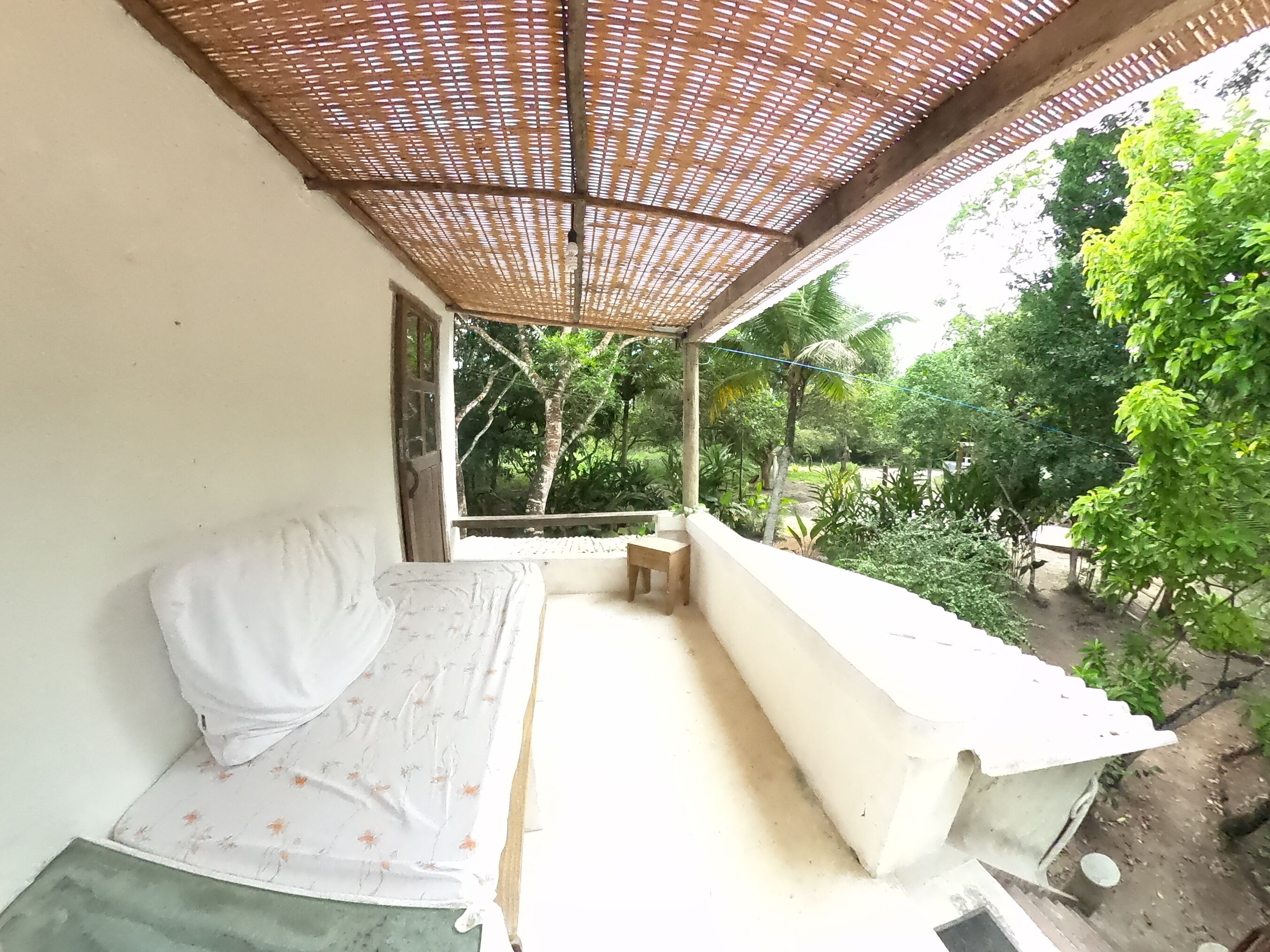 Een balkon met een bed, een tafeltje en uitzicht op groen.