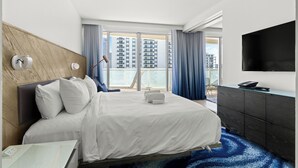 Ein Hotelzimmer mit einem großen Bett, einem Schreibtisch, einem Flachbildfernseher und Blick auf hohe Gebäude.