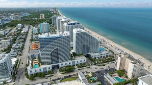 Ein Hochhaus-Hotel mit geschwungener Fassade, direkt neben einem Strand mit freiem Blick auf den Ozean.