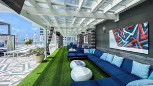 Eine Dachterrasse mit blauen Sofas, einer Fläche mit künstlichem Rasen und einem großen, abstrakten Wandbild.