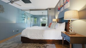 A modern bedroom with a large bed, a nightstand, a lamp, and a ceiling fan.