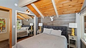 Een slaapkamer met een groot bed, twee nachtkastjes met lampen, een houten plafond en een hertenhoofd aan de muur.