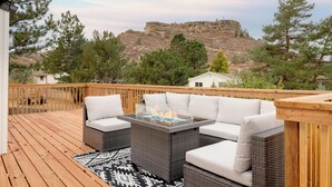 A deck with wicker furniture, a glass-top table, and a view of a rocky hill. - Updated & Spacious 5-bedroom house with Views of the Rock and Mountains  (Castle Rock)