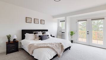 Une chambre à coucher avec un grand lit, une table de chevet, une commode, une fenêtre et une porte donnant sur un balcon.
