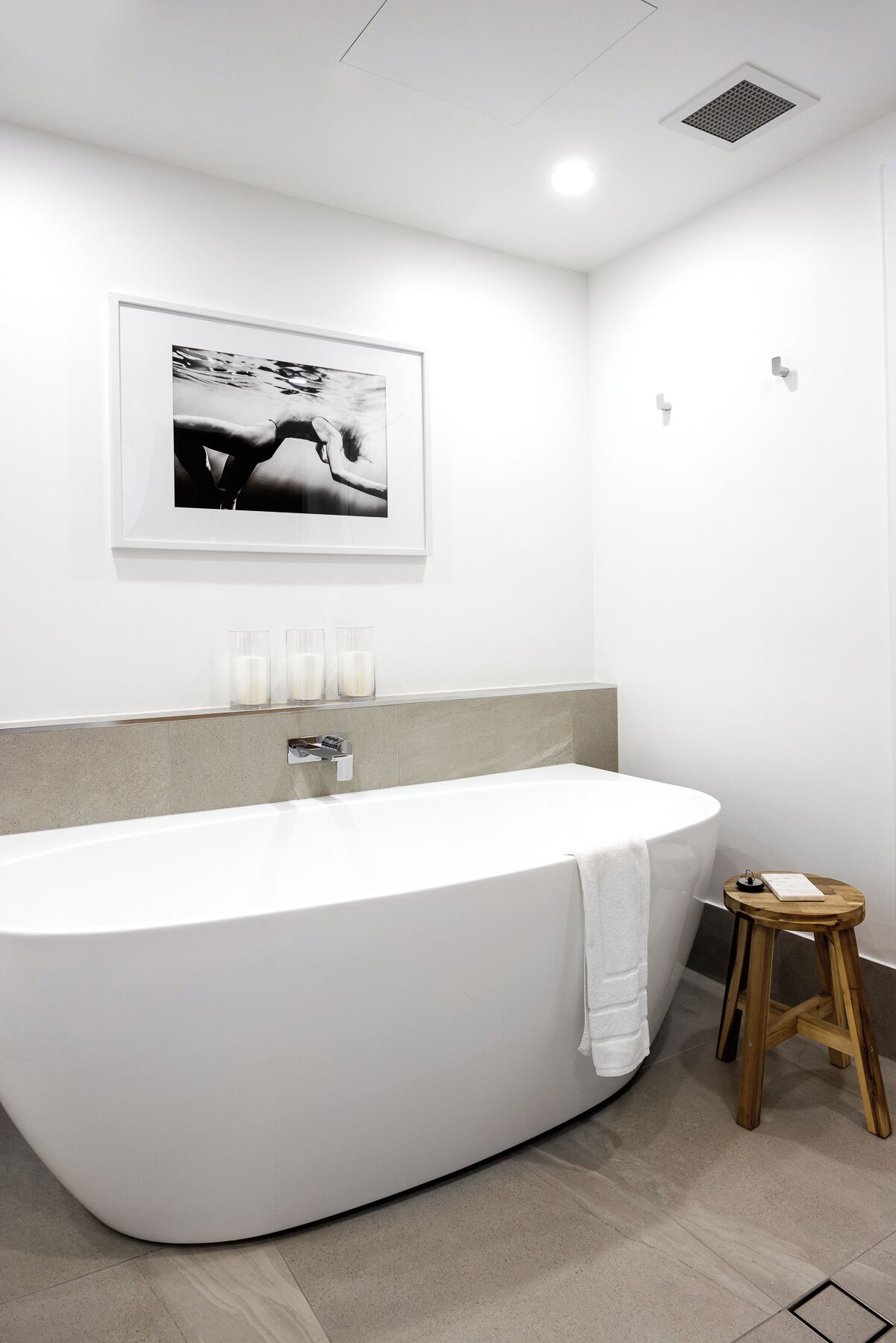 A modern bathroom with a freestanding bathtub, a framed photograph on the wall, and a small wooden stool.