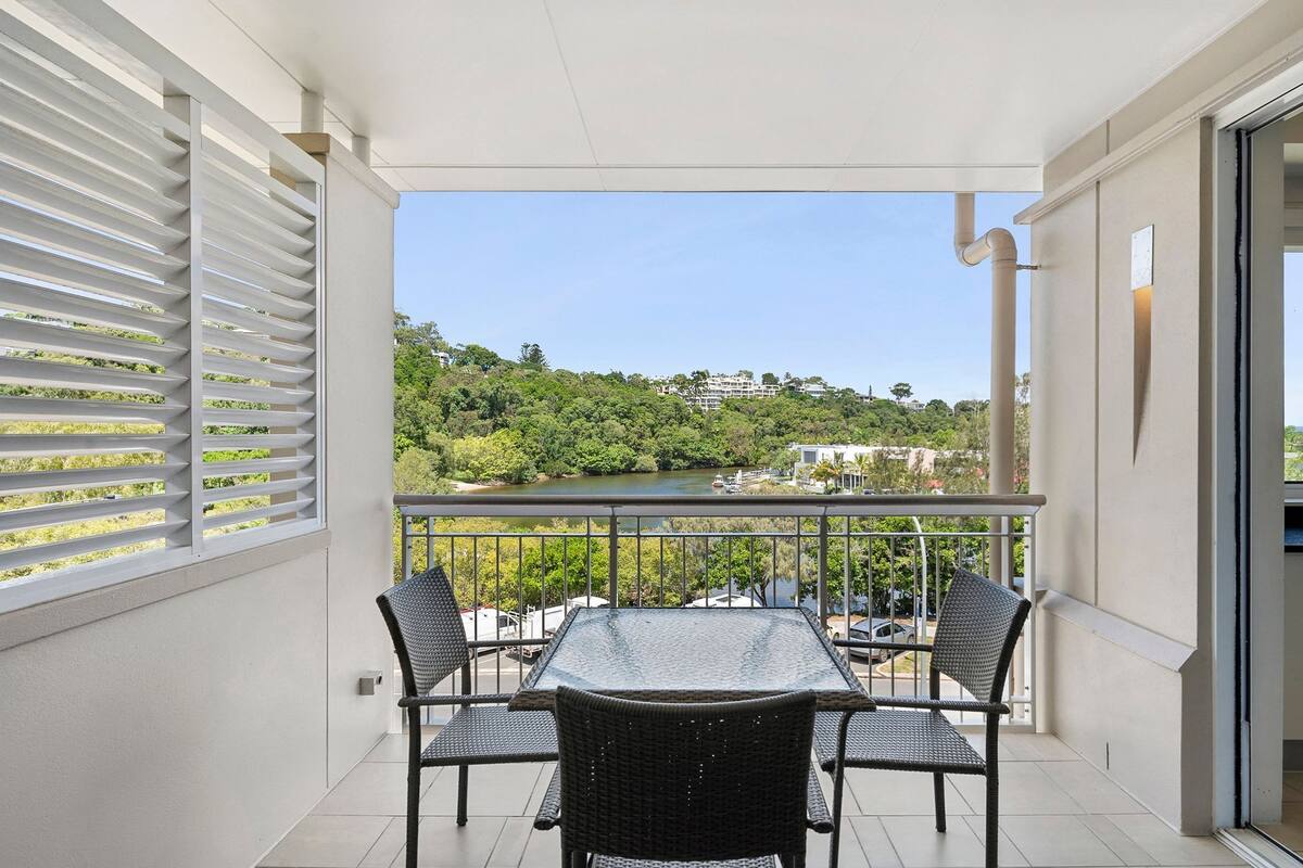 A balcony with a table and chairs, overlooking a river and greenery.