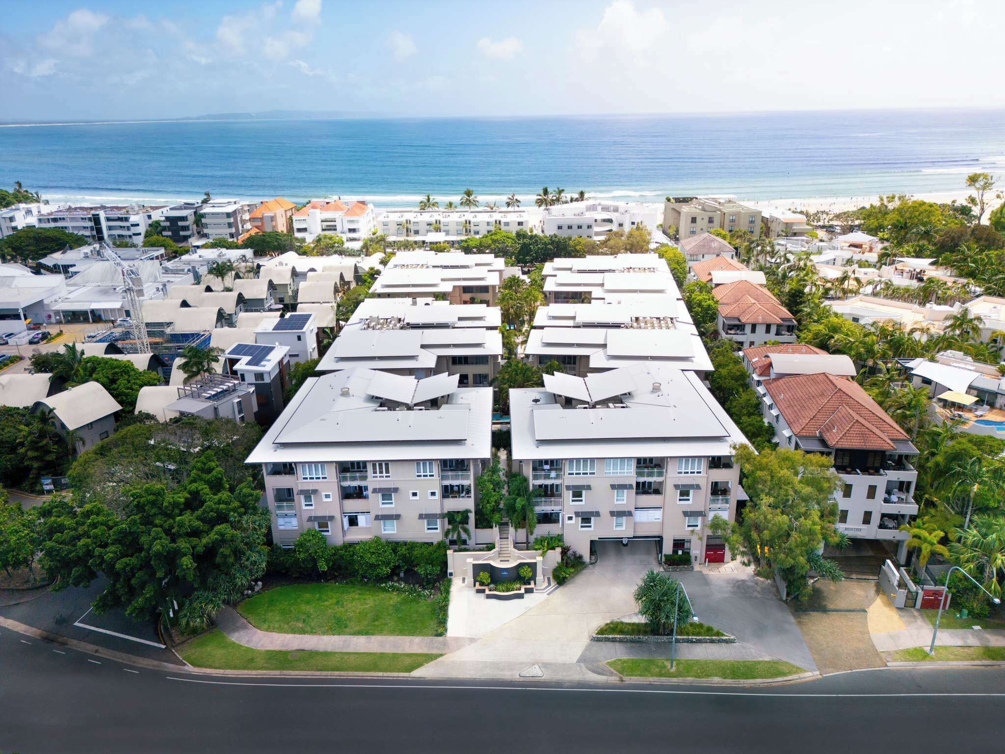 A high-rise hotel with multiple balconies, a parking lot, and a view of the beach and ocean.