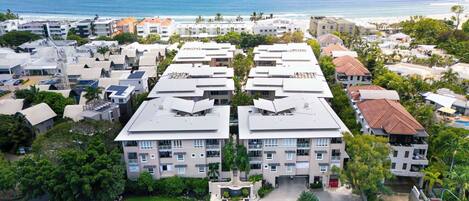 A high-rise hotel with multiple balconies, a parking lot, and a view of the beach and ocean.