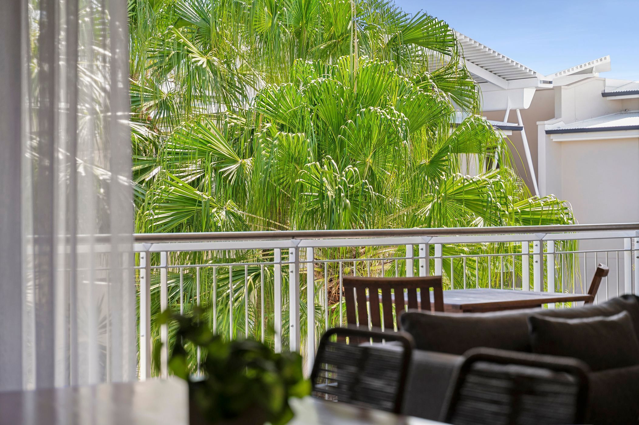 A balcony with a white railing, a wooden table, and a brown chair.
