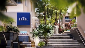 A hotel entrance with a blue sign, a water feature, and a staircase leading to the building. - Hastings Suites by Stay Noosa (Noosa Heads)