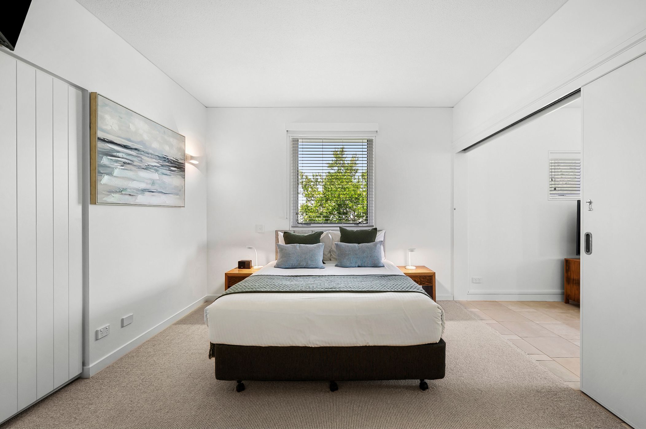 Un dormitorio moderno con una cama grande, una ventana con persianas, un cuadro en la pared y un armario.