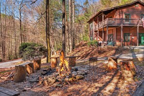 A rustic cabin with a fire pit surrounded by wooden benches and a porch.