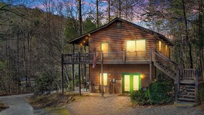A two-story log cabin with a balcony, a staircase, and a gravel driveway. - Relax to Creek Sounds • Hot Tub Cabin • Firepit BBQ (Cherry Log)