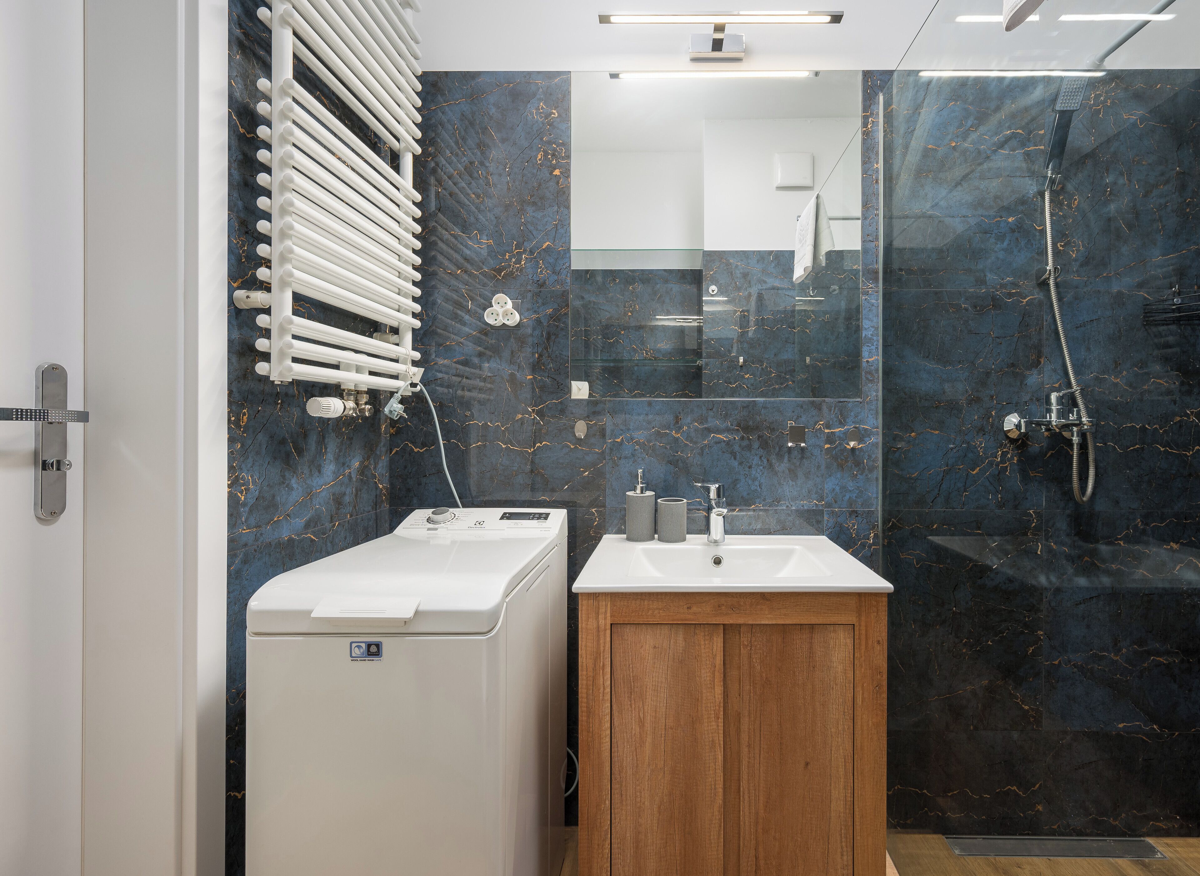 Un bagno moderno con lavatrice integrata, un mobile bagno in legno e cabina doccia in vetro.